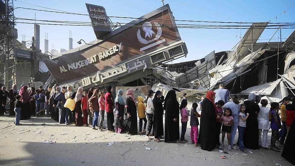 Gente haciendo fila en una panadería cuyo frente fue destruido por los bombardeos israelíes