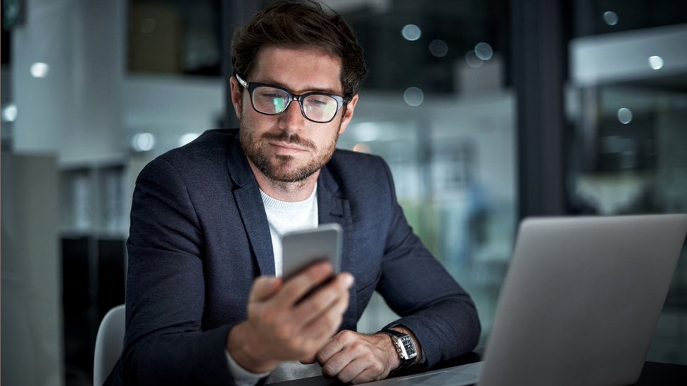 Un hombre mira su teléfono y computadora