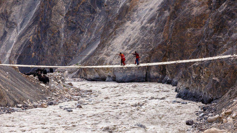 Varias pastoras cruzan un puente colgante de madera