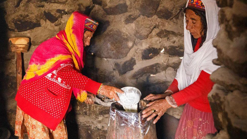 Dentro de sus cabañas, Annar (izquierda) y Thai Bibi (derecha) vierten yogur en un tambor tradicional para hacer mantequilla.