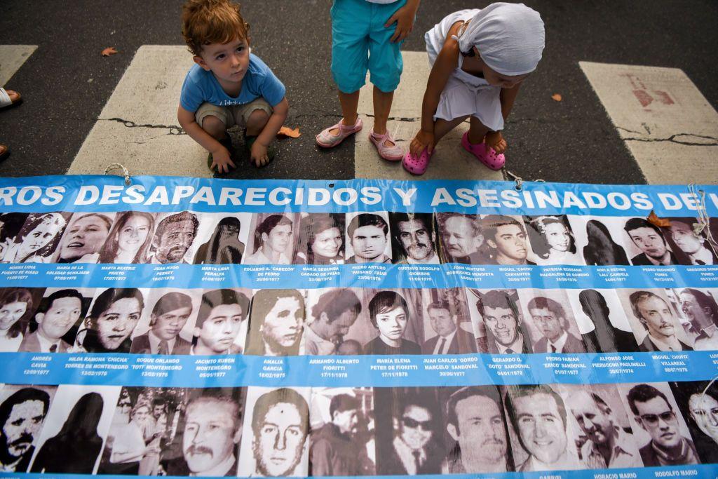 Niños juegan al lado de un cartel con imágenes y nombres de desaparecidos