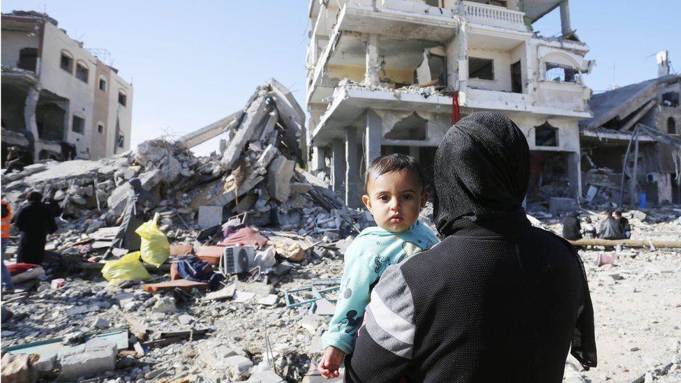 Un niño y un adulto ante un edificio en ruinas en Gaza.