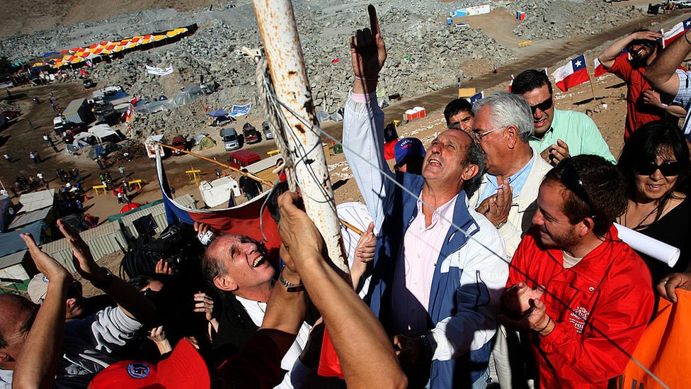 Dos sobrevivientes del accidente aéreo izan una bandera junto a la bandera que representa a los 33 mineros chilenos atrapados en una cueva en 2010.