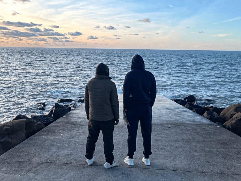 Dos jóvenes de espaldas miran al mar en que se ahogó Obada. 