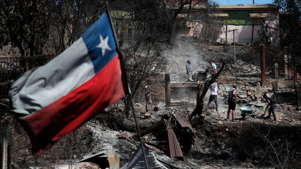 Una bandera chilena en medio de los restos de casas calcinadas.