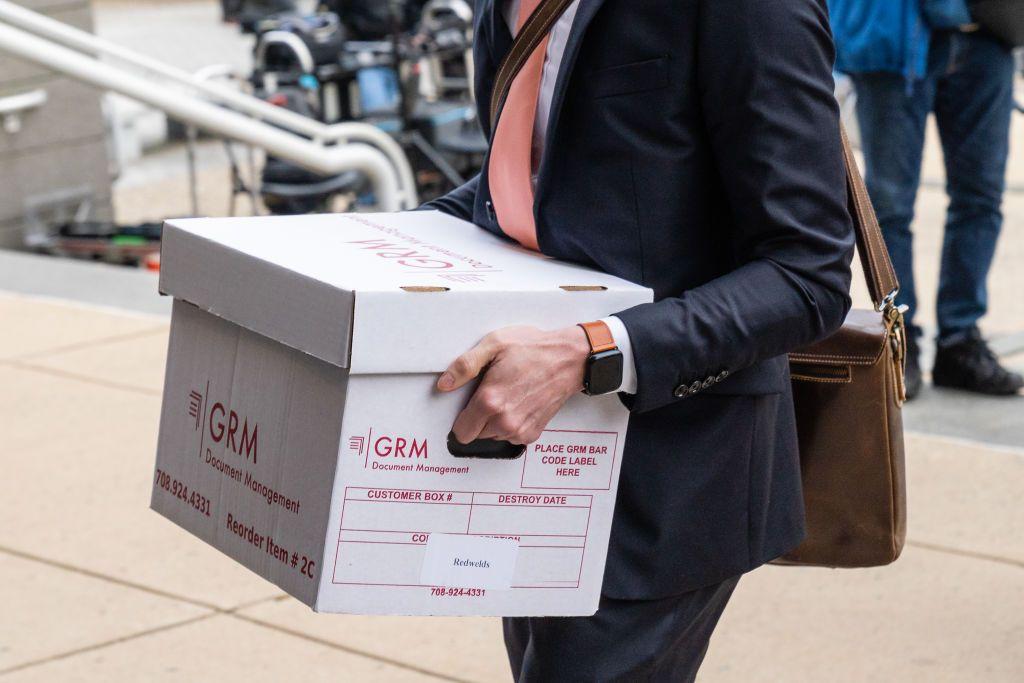 Un hombre en traje cargando una caja de documentos.