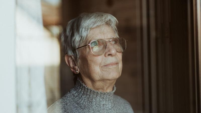 Una mujer mayor contemplando por la ventana