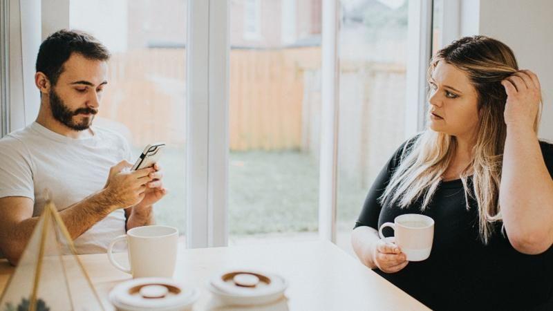 Una mujer mira a su pareja, que observa su celular