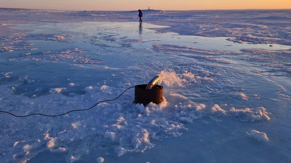 Bomba de agua de mar en acción con la puesta de sol ártico al fondo