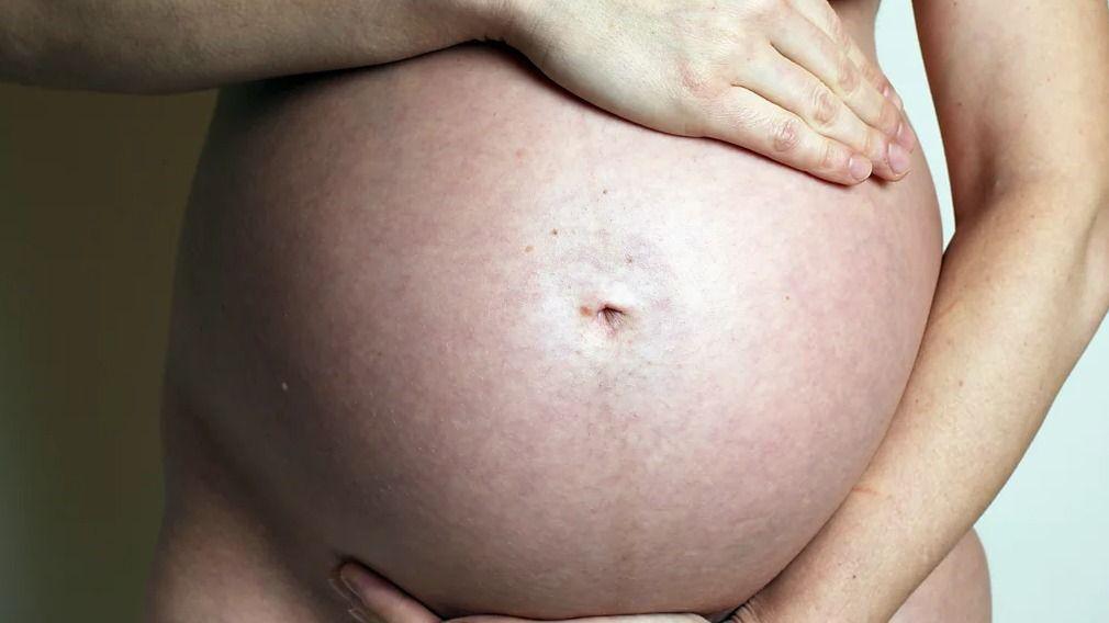 Una mujer embarazada colocando sus manos sobre su barriga.