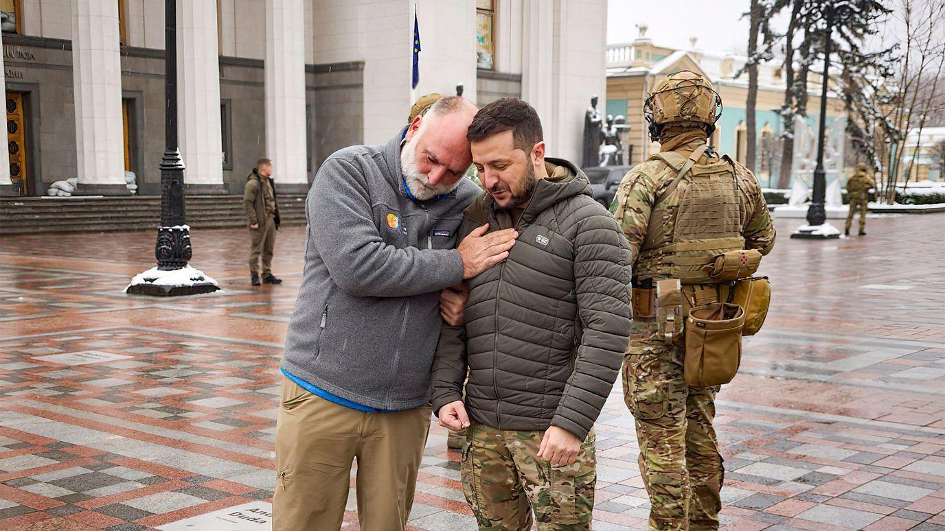 Andrés se apoya con una mano en el pecho del presidente de Ucrania, con soldados ucranianos en segundo plano.