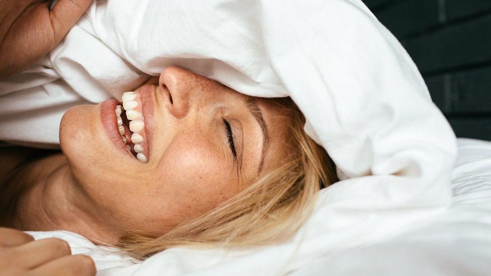 Una mujer sonriendo entre las sábanas