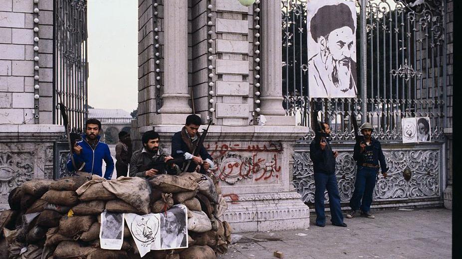 Soldados y hombres armados, hacen guardia junto a un edificio de Teherán con un poster de Jomeini colgado al fondo