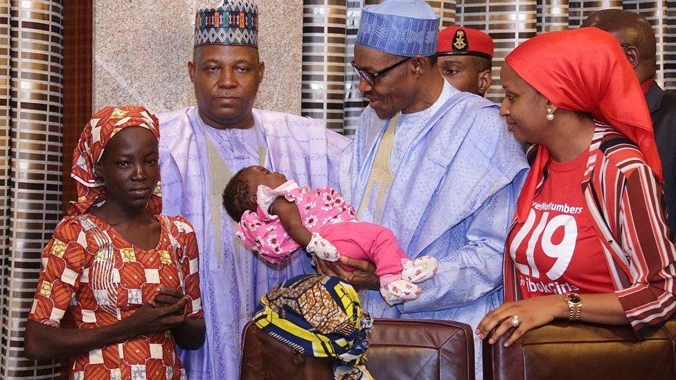 El presidente nigeriano Mohammadu Buhari (centro), flanqueado por el gobernador del estado de Borno, Kashim Shettima (i), y el jefe de gabinete del gobernador del estado de Kaduna, Hadiza Bala Usman (derecha), lleva al bebé de cuatro meses de Amina Ali a su llegada a la presidencia en Abuja. el 19 de mayo de 2016