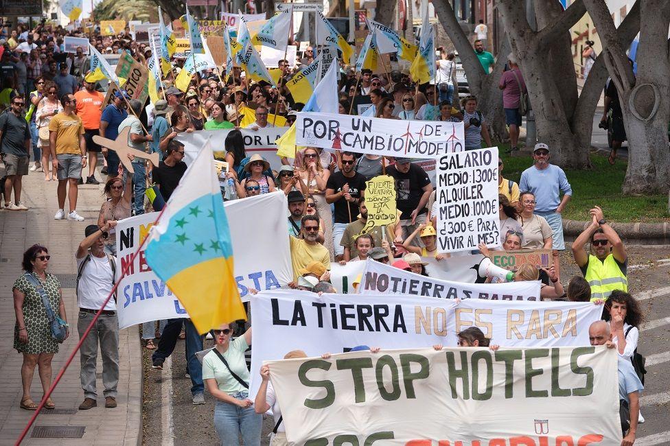 Manifestantes en las calles con pancartas y banderas. Un pancarta dice: Stop hotels