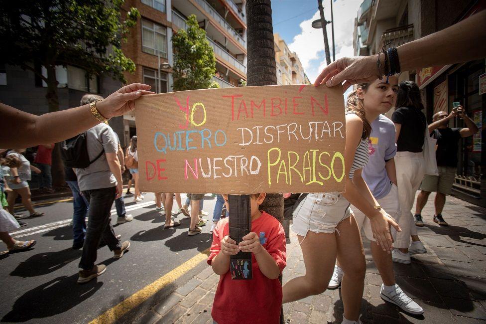 Un niño con una pancarta que dice: Yo también quiero disfrutar de nuestro paraíso