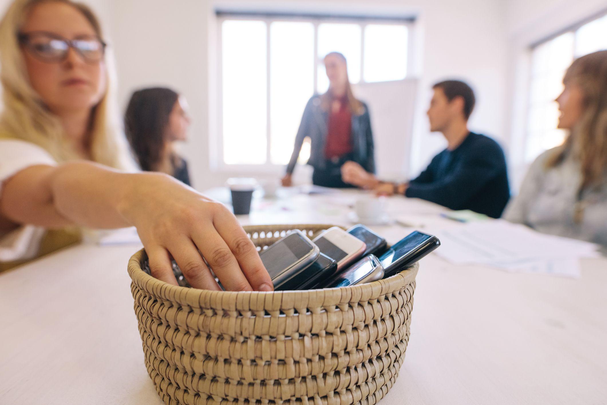 Un grupo de personas reunidas alrededor de una mesa sobre la cual hay una canasta en la que hay varios celulares