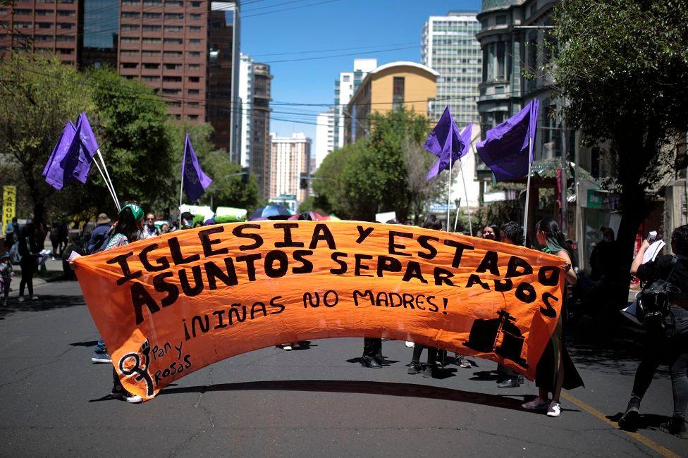 Mujeres con una pancarta gigante que dice: "Iglesia y Estado, asuntos separados. Niñas no madres"
