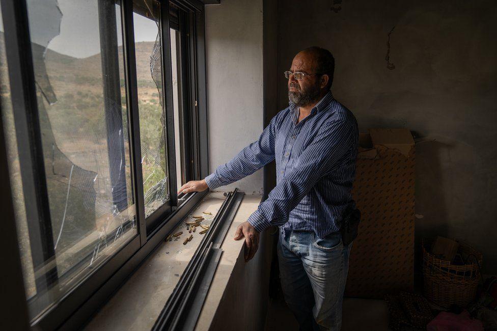 Abdellatif mira desde una de las ventanas rotas de su casa. En frente, están los cartuchos recolectados de las balas disparadas por los colonos