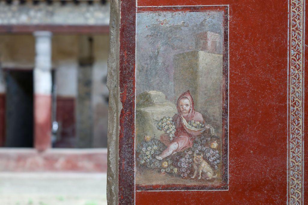 Fresco de un niño encapuchado con un perro a su lado.