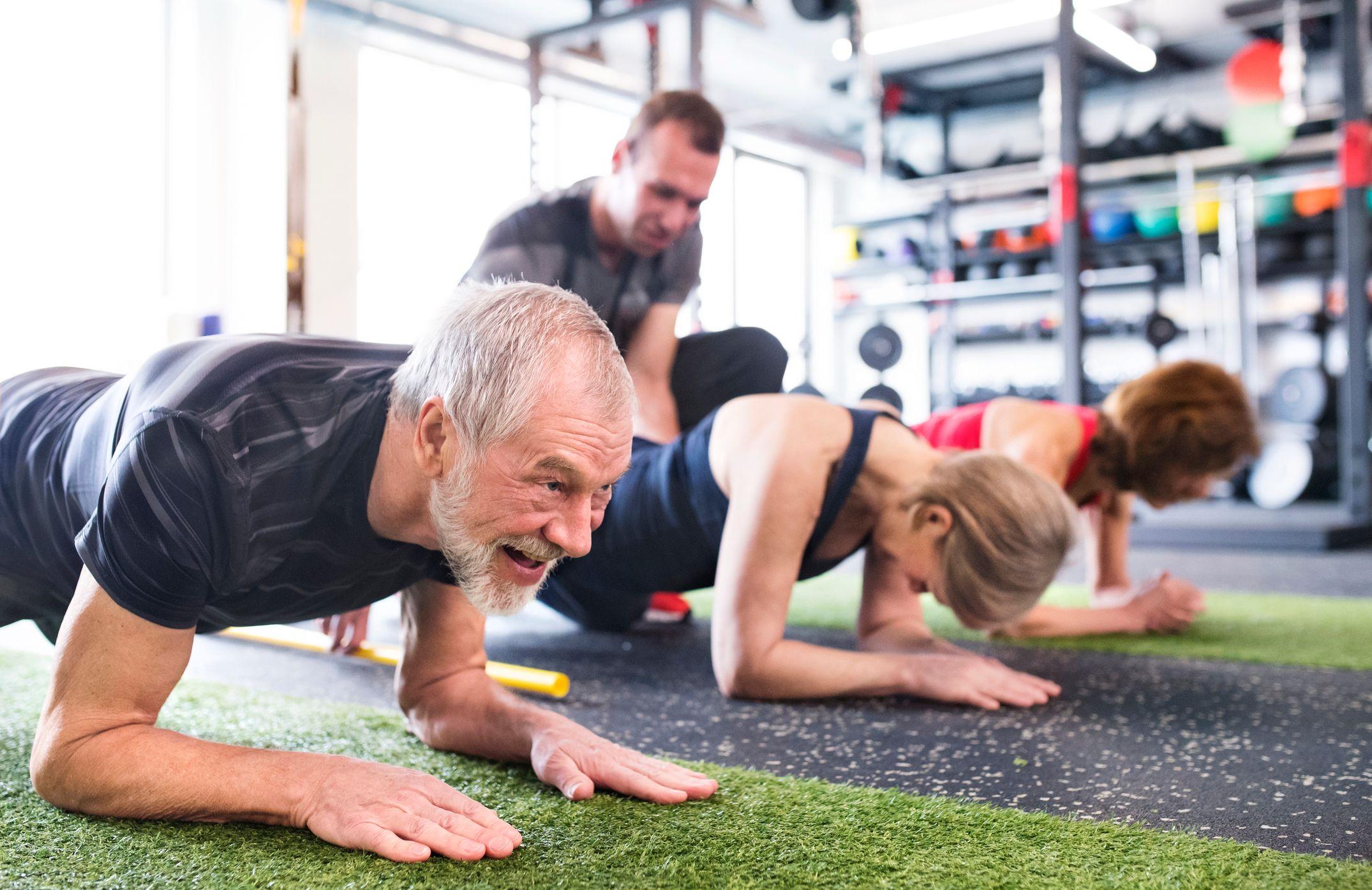 Personas mayores haciendo planchas en gimnasio.