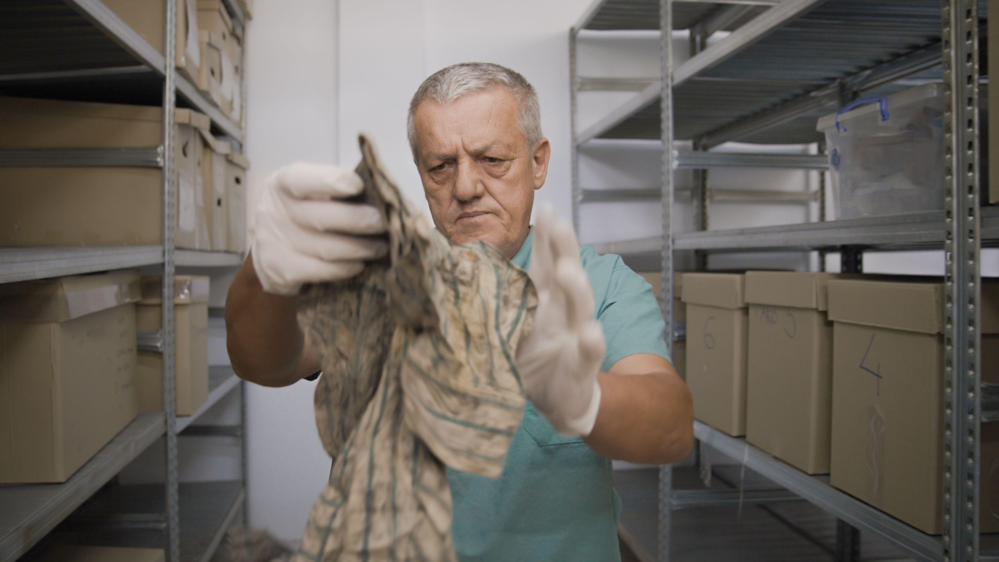 El doctor Arsim Gerxhaliu inspecciona una prenda de vestir encontrada en una de las fosas comunes.