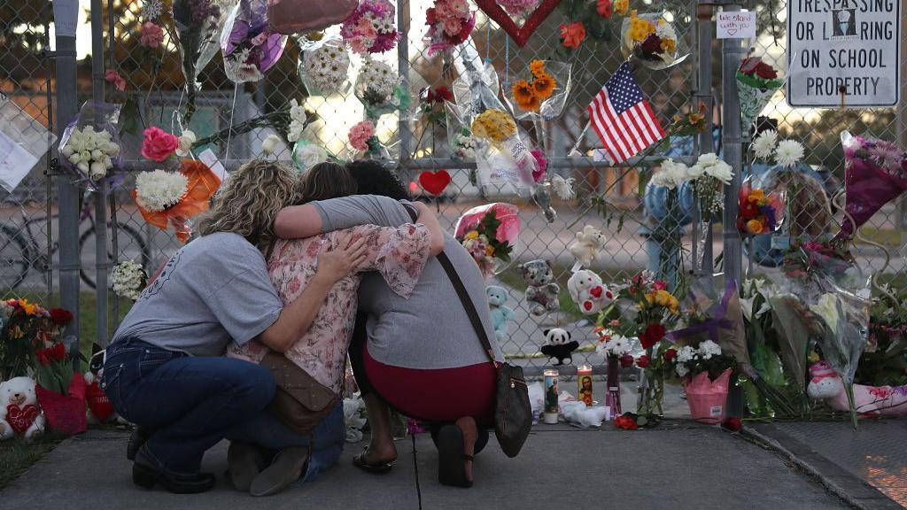 Mujeres se abrazan frente a una pared de recuerdos en honor a víctimas del tiroteo de Marjory Stoneman Douglas