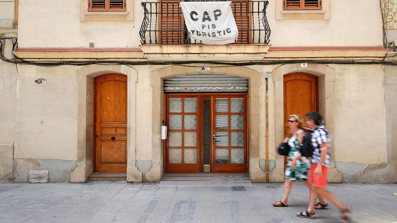 Una pareja pasa frente a una residencia con una aviso que lee en catalán: "No hay pisos turísticos"