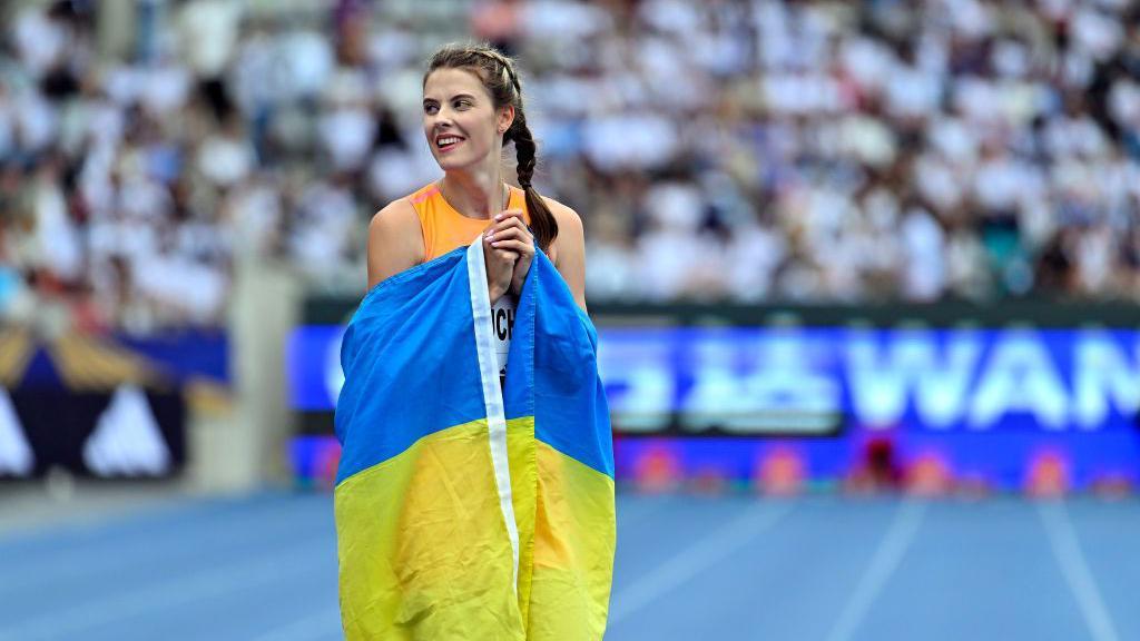 Yaroslava Mahuchikh en la pista de atletismo abrazando la bandera de Ucrania