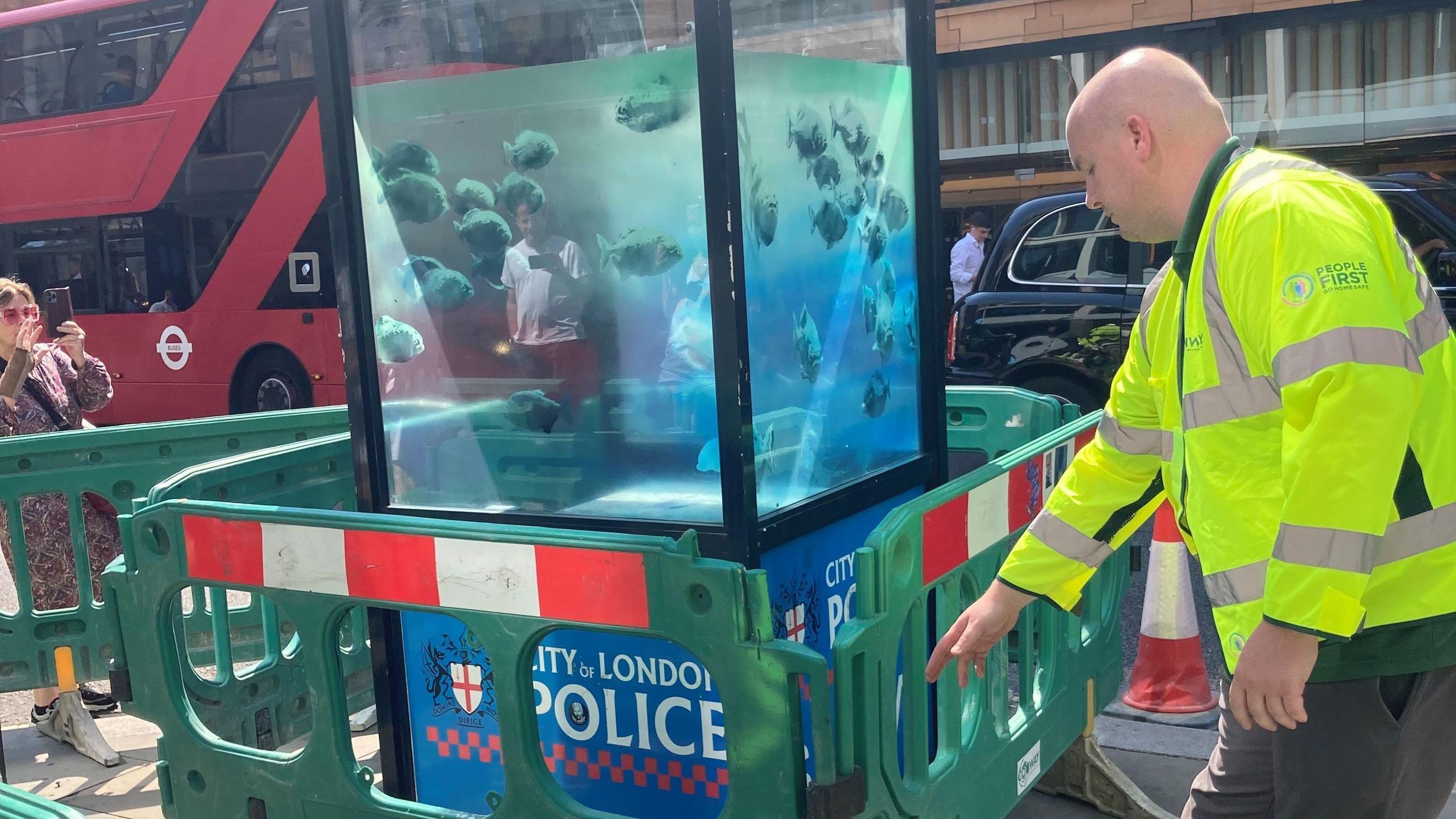 Un policía de la City de Londres frente a una caseta de policía con el grafiti de pirañas