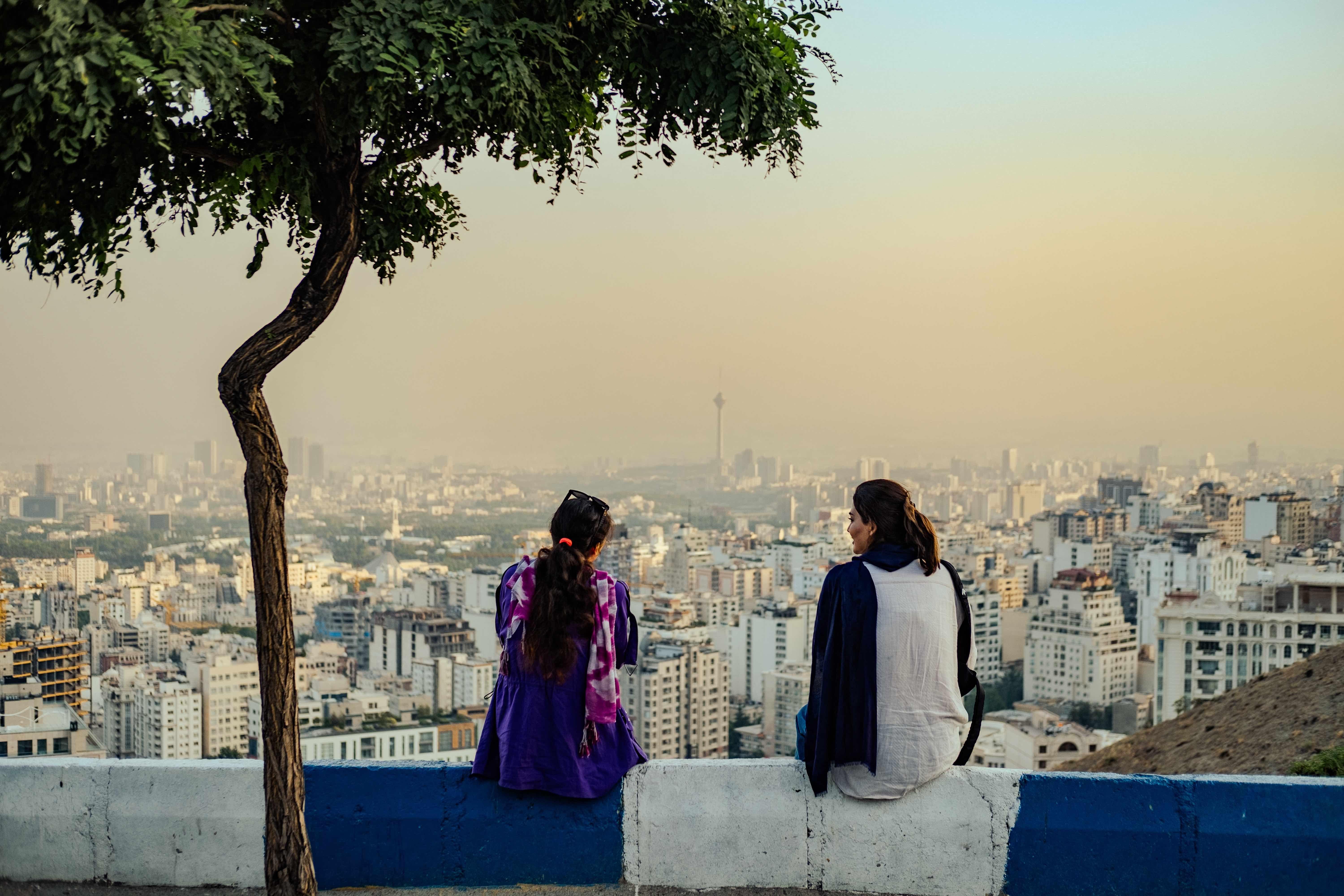 Mujeres iraníes sin hiyab obligatorio sentadas con vistas a la ciudad de Teherán, 2024.