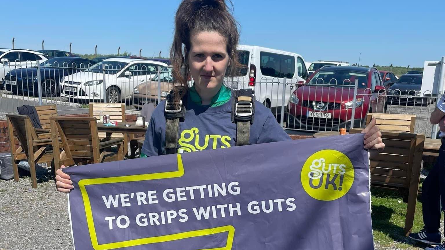 Luned Davies sostiene una pancarta de la caridad Guts UK tras haber hecho un salto en paracaídas 