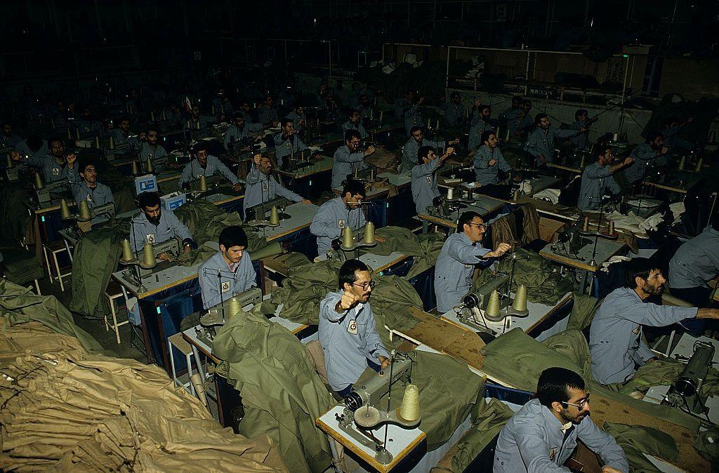 Presos políticos iraníes, con los puños en alto, corean consignas de propaganda en apoyo de la República Islámica, mientras confeccionan ropa, en la prisión de Evin en 1986.
