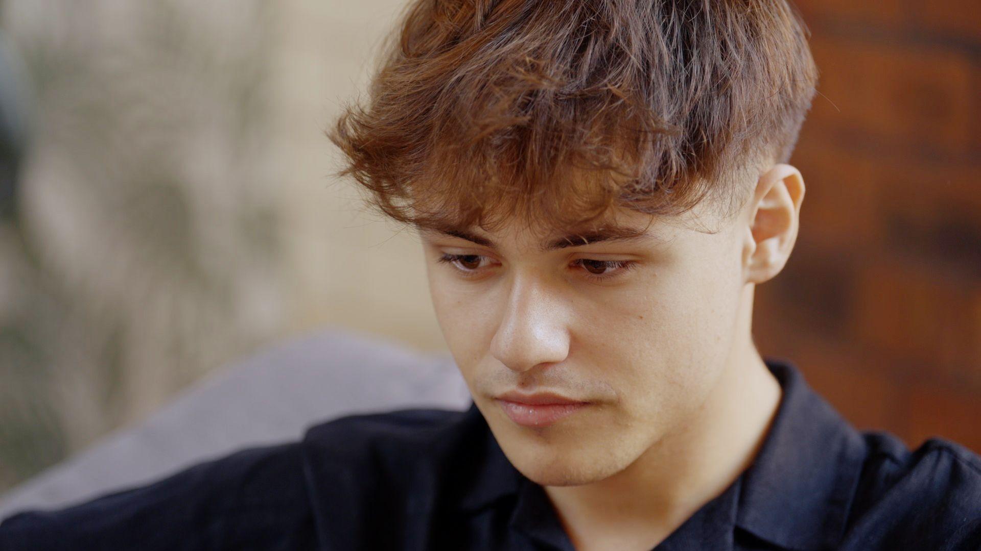 Cai, un joven con una camisa negra y mirada pensativa