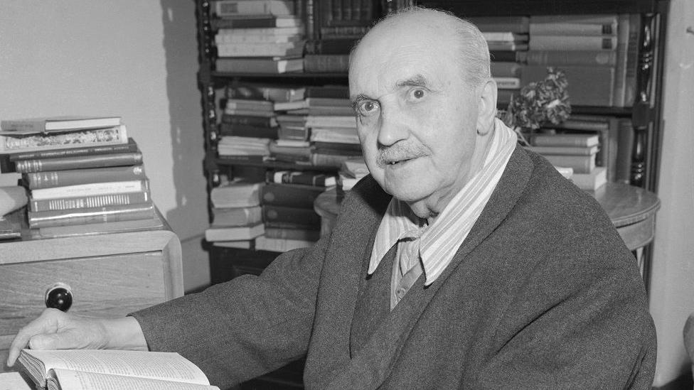 George Santayana con un libro en la mano y una biblioteca de fondo