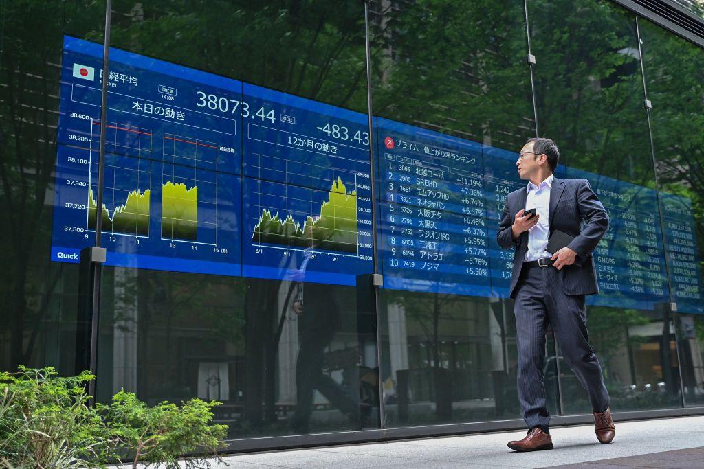 Un hombre camina junto a un panel con información bursátil en Tokio.