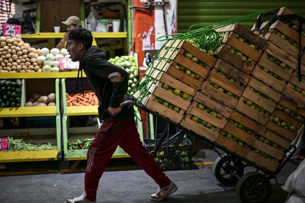 Un mozo arrastra un carro con mercancía en un mercado de México.