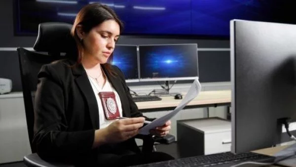 Agente de ciberseguridad de la PDI mirando un informe y revisando un computador personal.