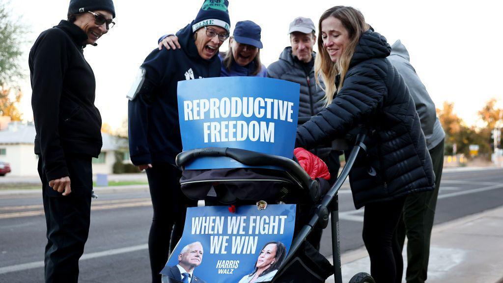 Julie Bufkin (derecha) conversa con los vecinos mientras empuja el cochecito de su hija Alice, adornado con carteles que dicen "Libertad reproductiva" y "Cuando luchamos, ganamos", el 5 de noviembre de 2024 en Tempe, Arizona. La aprobación de la Proposición 139 en Arizona codificaría “el derecho fundamental al aborto” en Arizona. (Foto de Mario Tama/Getty Images)