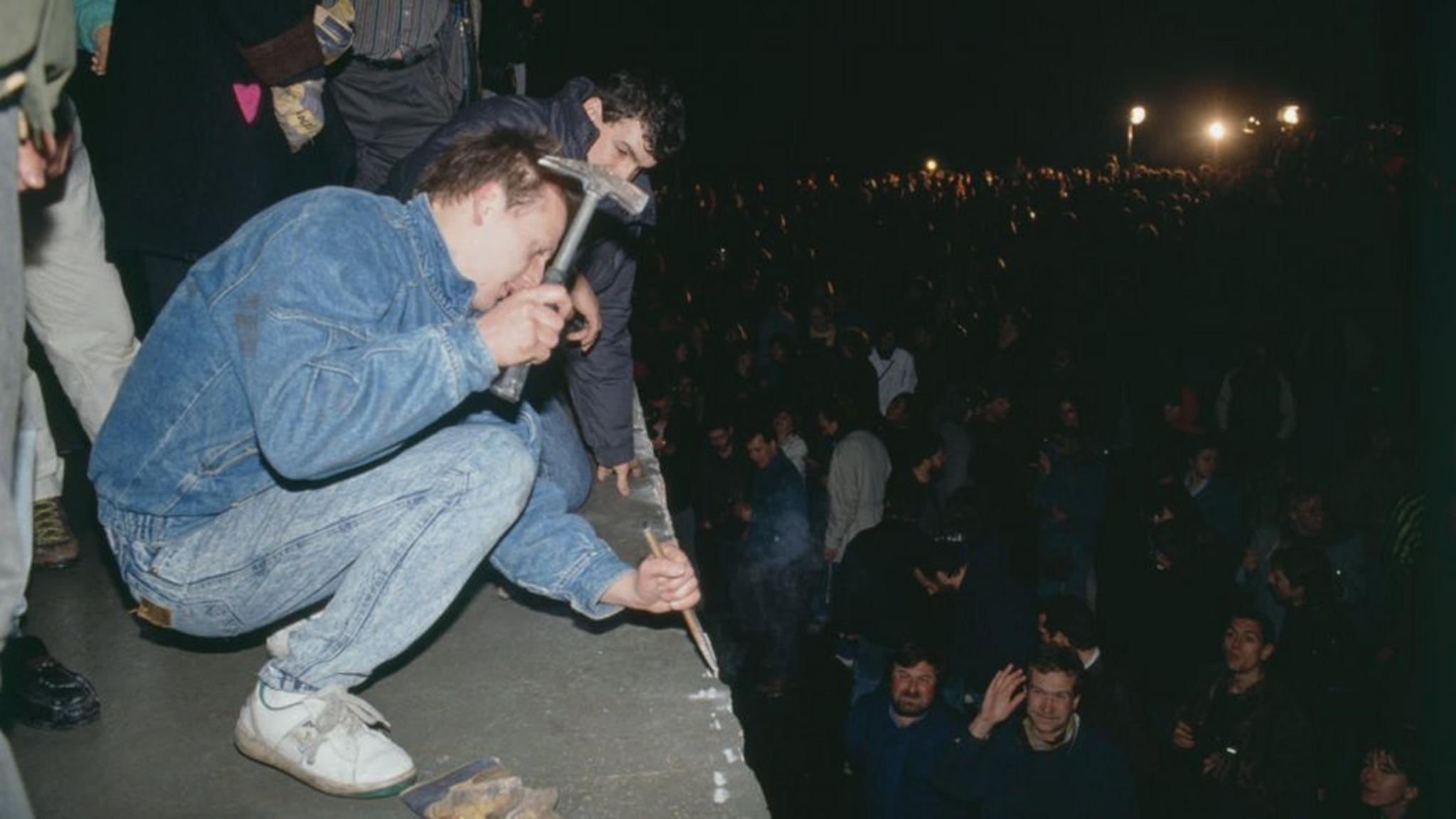 Un joven golpea con un martillo y un cincel el Muro de Berlín