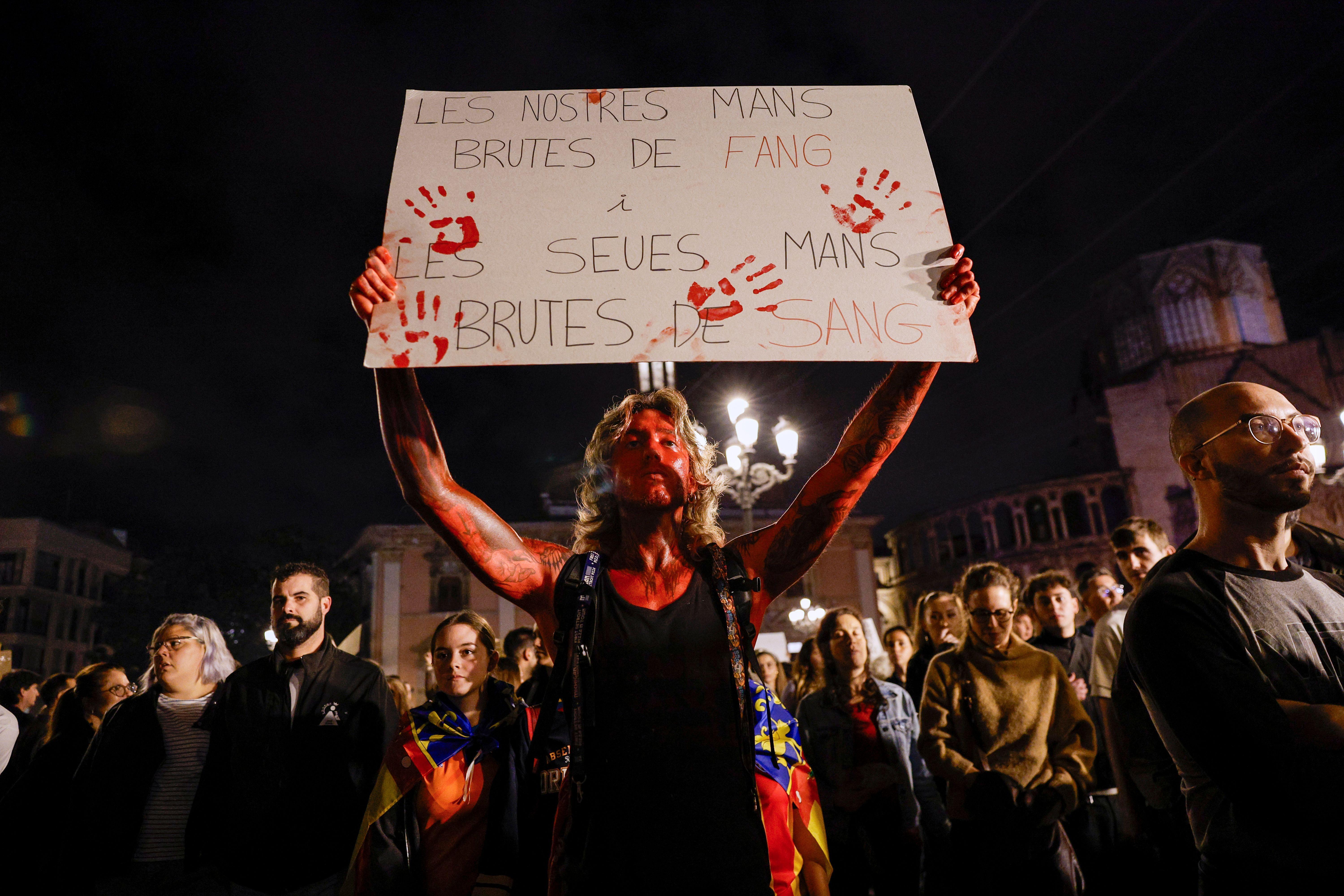 Una persona con pintura roja en el cuerpo carga una pancarta que lee: "Nuestras manos manchadas de barro, las suyas de sangre".