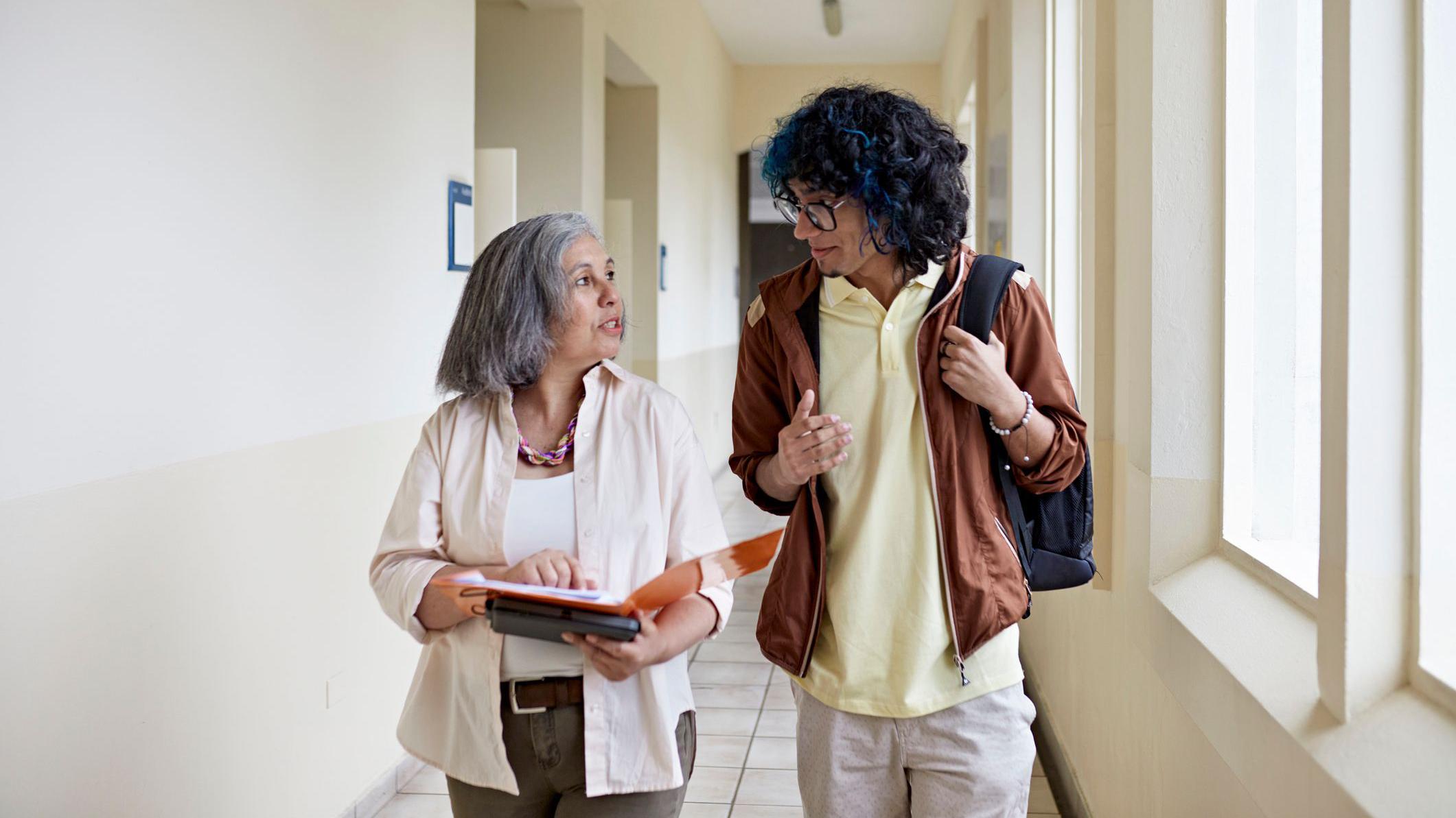 Profesora y alumno conversando en un pasillo.