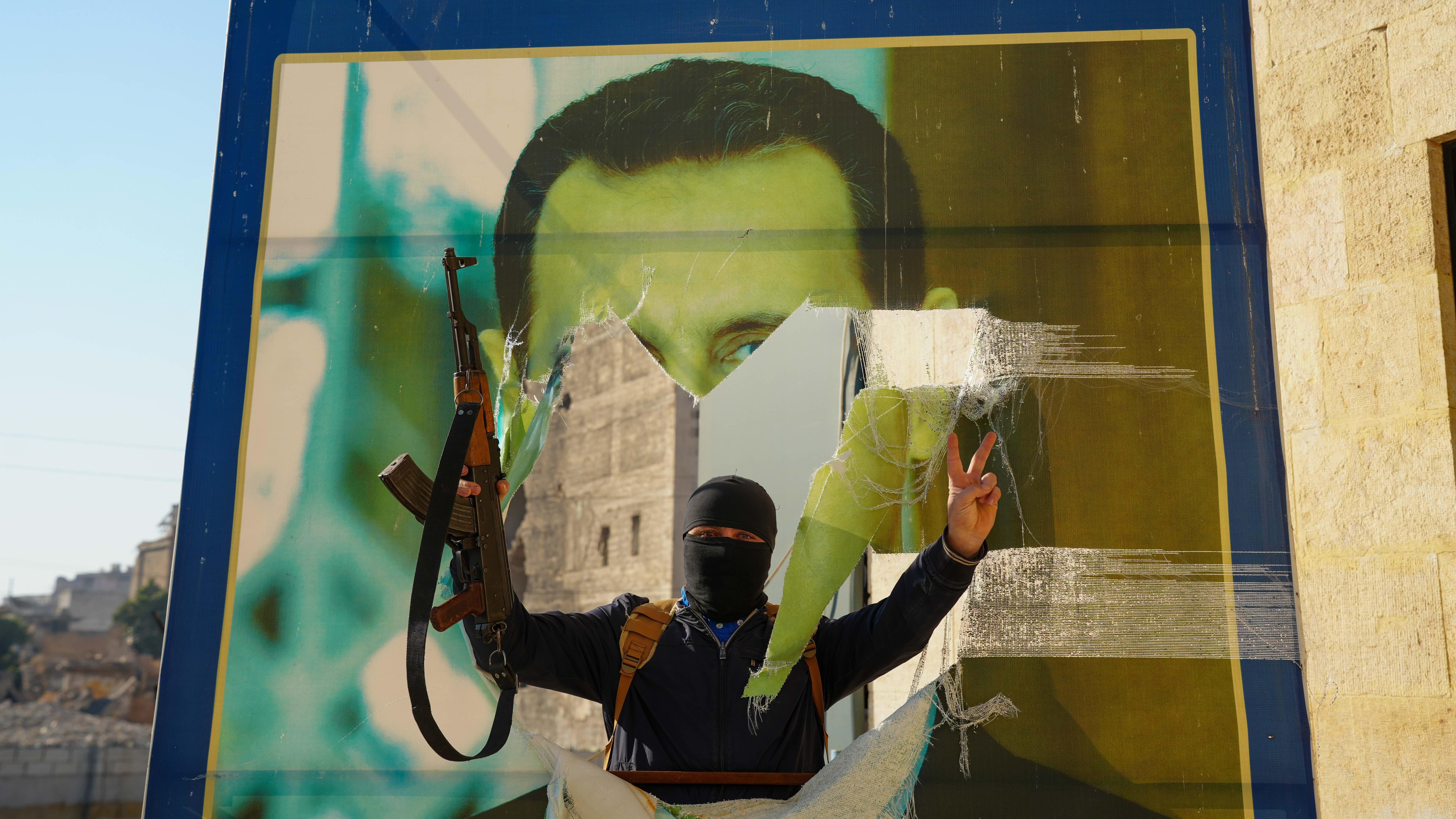 Un rebelde aramado hace una señal de victoria frente a una pancarta rota del presidente al Assad
