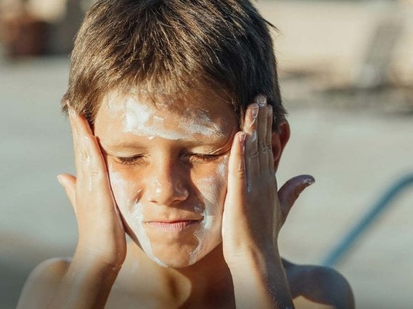 Una playa con turistas aplicando protector solar, con el mar de fondo, resaltando el impacto de los químicos en el agua.