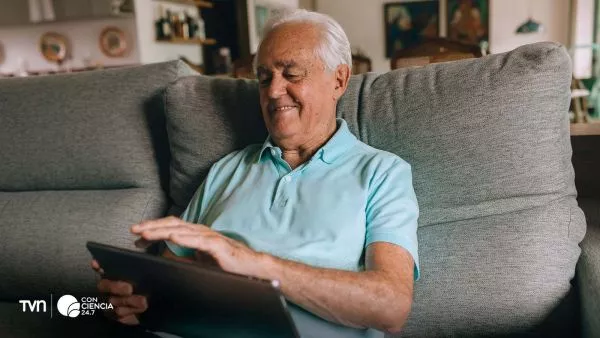 Persona mayor usando un smartphone en casa, concentrada y sonriente, como símbolo del vínculo positivo entre tecnología y salud cognitiva.