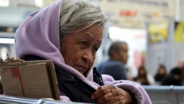 Adulta mayor envuelta en un polerón morado, sosteniendo un cartón