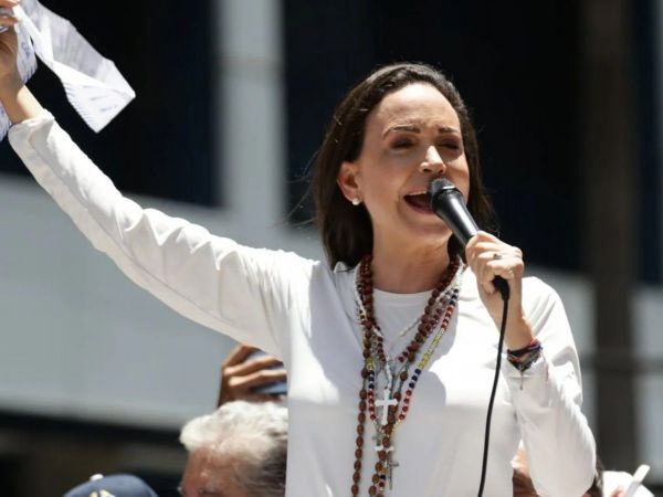 María Corina Machado, vestida de blanco, hablando en público con un micrófono en la mano izquierda y un papel en la mano derecha