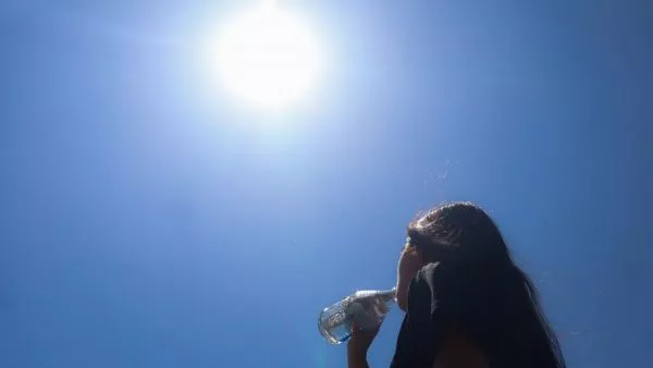 Mujer de espaldas a la cámara bebiendo una botella de agua bajo el sol