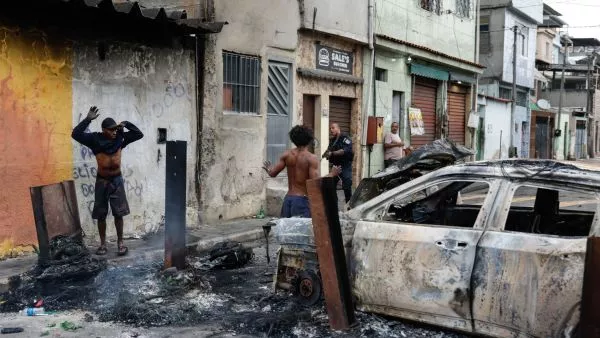 Policía con arma en la calle, auto quemado y hombres con los brazos arriba en medio de operativo.
