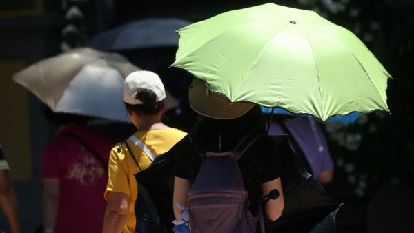 Personas con sombrillas bajo el calor.